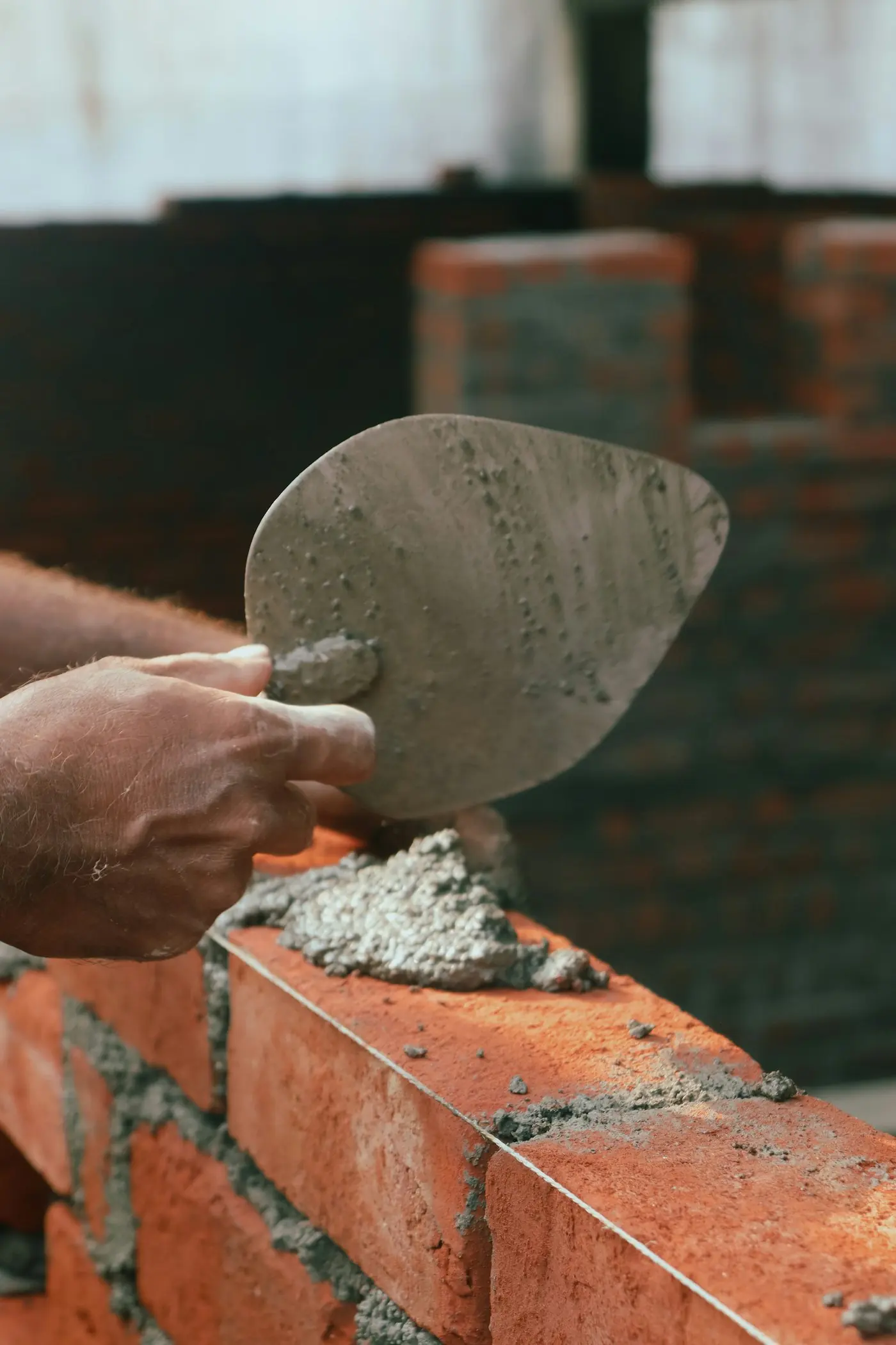 A bricklayer's trowel bedding mortar on a new brick course
